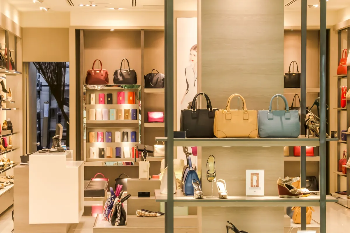 Luxusboutique mit Taschen in beleuchteten Nischen, aufgereihten Portemonnaies im Ständer und Pumps in den Regalen