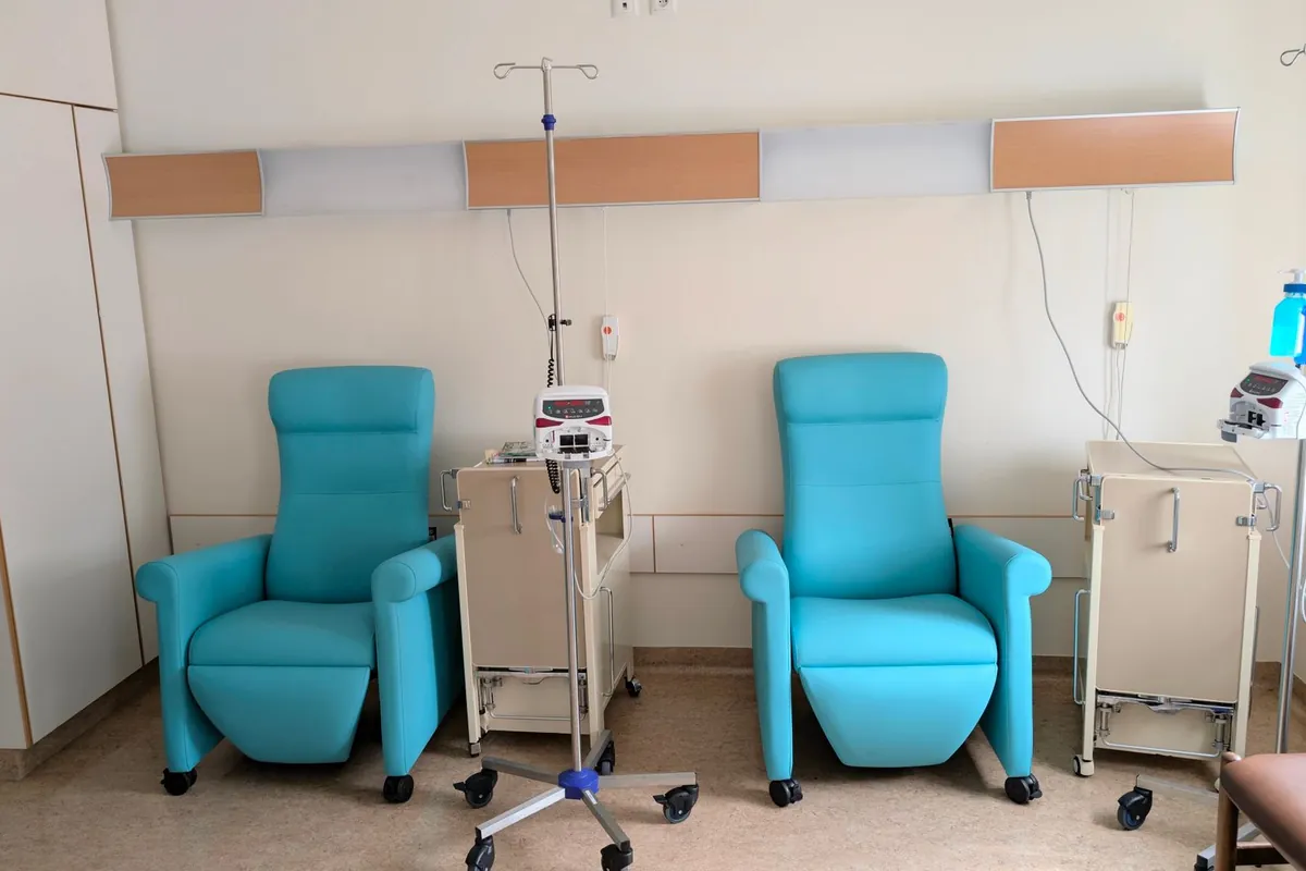 Sala di day hospital con due poltrone reclinabili per infusione, l'asta della flebo in mezzo e la pompa sul carrello