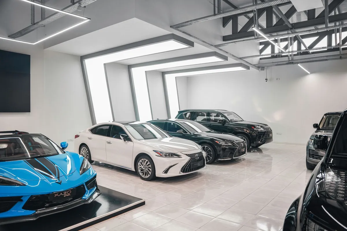 Showroom di una concessionaria con le auto allineate sul pavimento lucido e uno schermo spento appeso alla parete di fondo