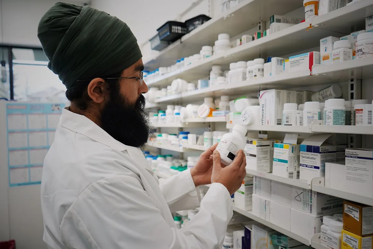 Farmacéutico con bata blanca cogiendo un frasco de una estantería de dispensación llena de cajas de medicamentos ordenadas por filas