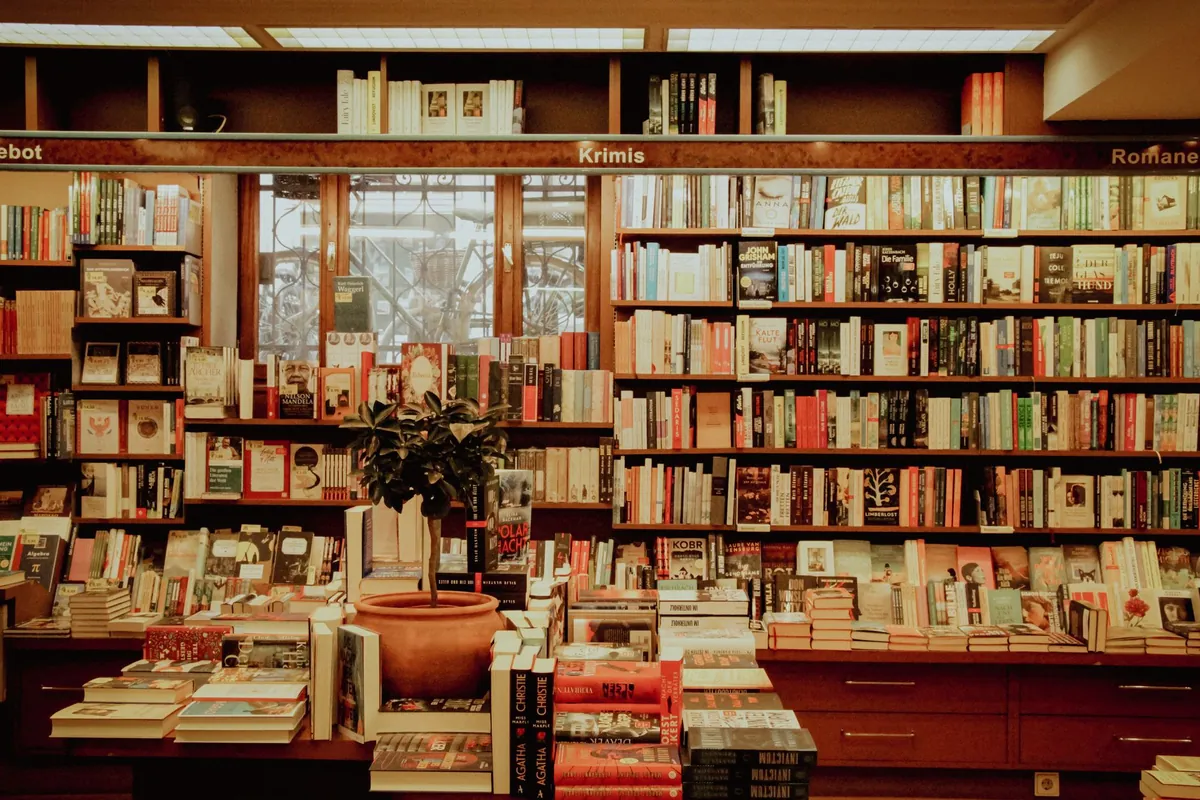 Bookshop interior with shelves covering the wall, tables of stacked new releases and section signs running above the shelves