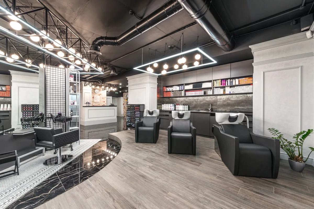 Friseursalon mit drei schwarzen Waschbecken in einer Reihe, einem Schneideplatz mit Spiegel und Produktregalen an der Wand