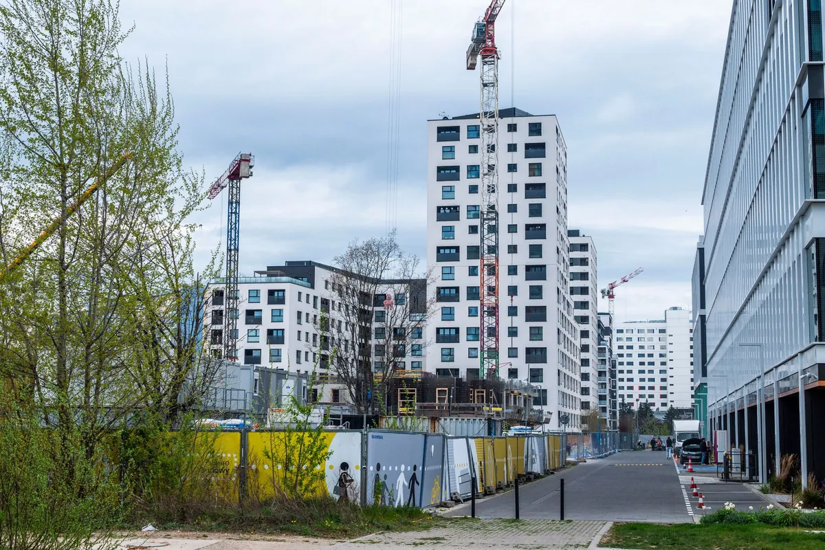 Empreendimento residencial em obras com duas torres pela metade, gruas e o tapume impresso ao longo da rua