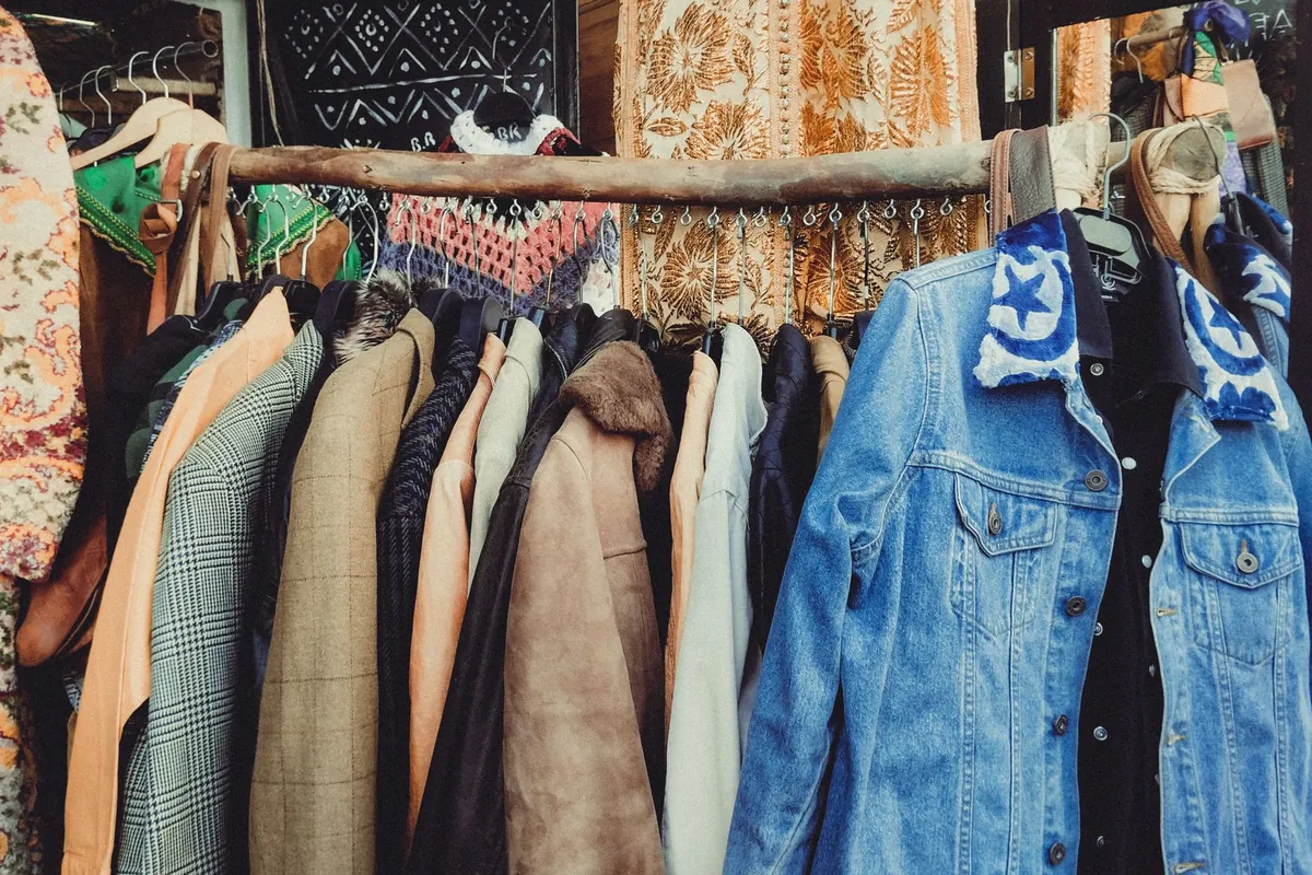 Portant de friperie avec des manteaux en laine, des vestes en jean brodées et des tissus imprimés derrière