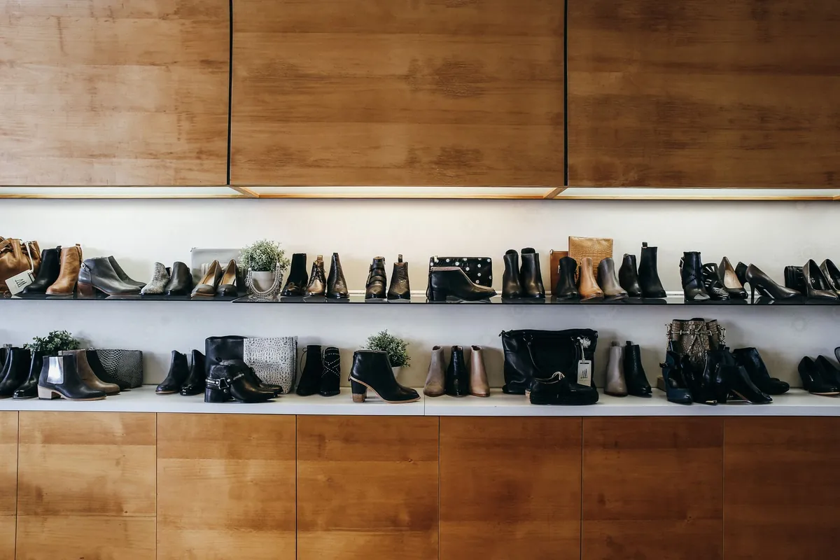 Shoe shop wall with two long shelves of ankle boots and heels above light wooden cabinets